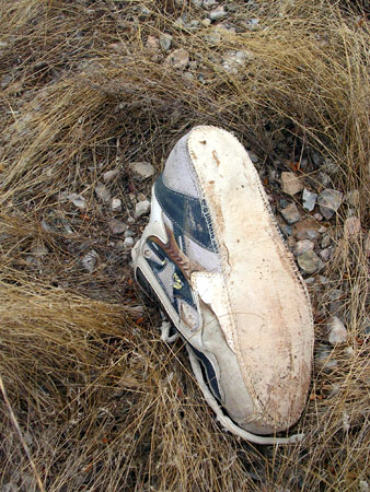 An immigrant's shoe at the Mile Marker 157 lay-up. Typical of shoes that have been walked on through the rough Sonoran Desert, the sole has fallen away, and the fabric in the upper has been torn by desert brush.