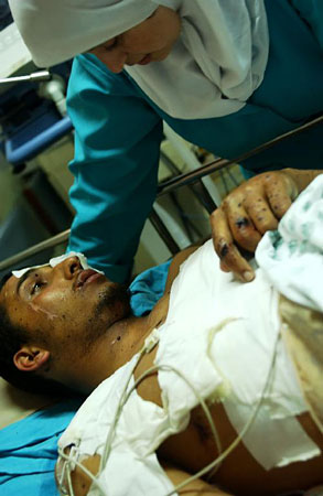 A Palestinian doctor with a man who lies in the Shifa Hospital ICU after being wounded in an Israeli air attack.