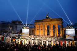 Tourists gather to see the individually painted dominos along the former route of the wall in front of illuminated landmark Brandenburg Gate in Berlin. Click image to expand.