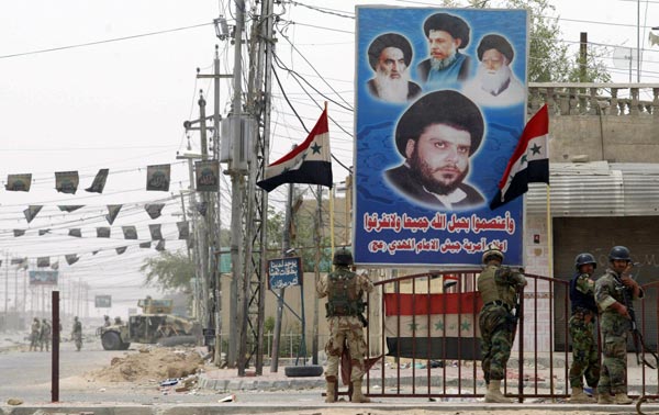 Iraqi soldiers stand under a poster of Moqtada al-Sadr.