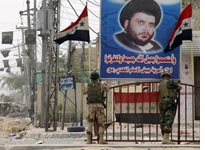 Iraqi soldiers stand under a poster of Moqtada al-Sadr. Click image to expand.