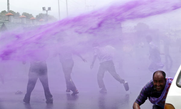 A water cannon sprays protesters with purple water.