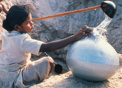 A young girl collecting water from holes dug in the ground.